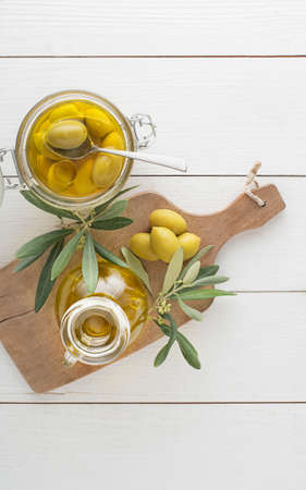 Olive oil bottle and olive branch with Pickled green olives in glass jar on the wooden tableの写真素材