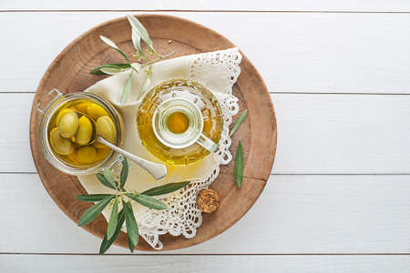 Olive oil bottle and olive branch with Pickled green olives in glass jar on wooden tableの写真素材