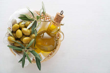 Olive oil bottle and olives with branch in basket on wooden tableの写真素材