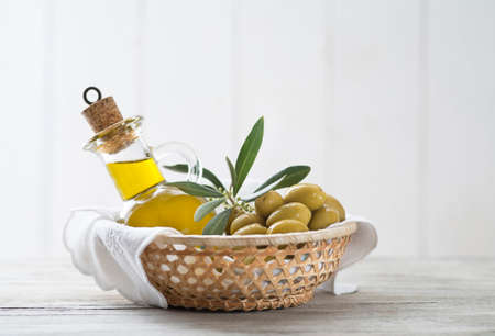 Olive oil bottle and olives with branch leaves in basket on wooden tableの写真素材