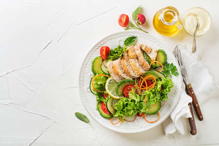 Healthy green salad with chicken breast and fresh vegetables on white tableの写真素材