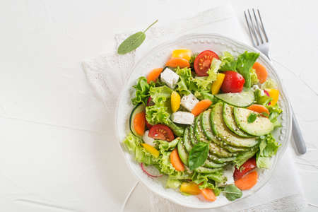 Healthy green salad with avocado, feta cheese and fresh vegetables on white background close upの写真素材