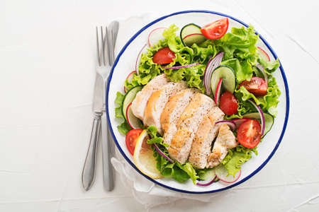 Healthy green salad with chicken breast and fresh vegetables on white table close upの写真素材