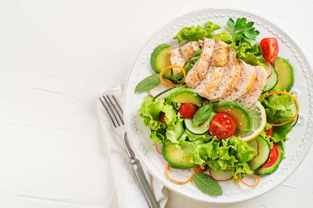Healthy green salad with chicken breast and fresh vegetables on white table close upの写真素材