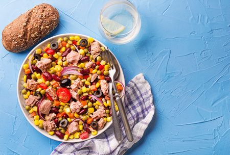 Healthy mixed tuna salad with corns, carrots, peas, beans and olives on blue table background. Mexican corn salad.の写真素材