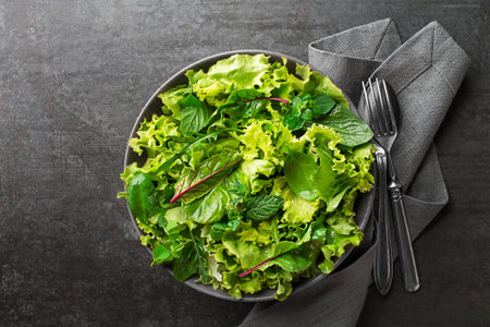 Fresh green leafy salad with herbs on dark table background. Concept for a tasty and healthy meal