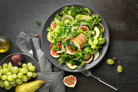 Fresh green leafy salad with fruits and nuts on dark table background. Concept for a tasty and healthy mealの写真素材