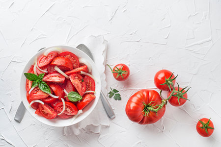 Fresh tomato salad with onion and basil on white table background. Concept for a tasty and healthy mealの写真素材