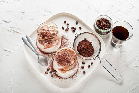 Traditional Italian dessert tiramisu in a glass cup. Homemade tiramisu in glass jars, step by step cooking process. Traditional unbaked italian dessert on white background. Coffee and mascarpone cream cake.の写真素材