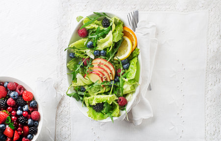 Healthy green salad with berry and apple fruit on white background. Fresh salad with fruit ingredients and greens. Healthy food.の写真素材
