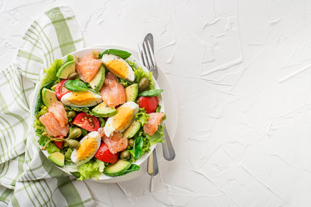 Fresh green lettuce salad with smoked salmon, cherry tomatoes, egg and avocado on white table backgroundの写真素材
