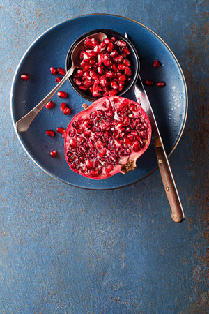Healthy ripe pomegranate fruit opened and splitted with seeds in cup on blue backgroundの写真素材