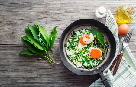 Fried eggs in a frying pan with fresh ramson or wild garlic leaves. Healthy spring diet food concept.の写真素材