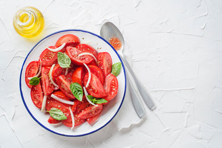 Fresh tomato salad with onion and basil on white table background. Concept for a tasty and healthy mealの写真素材