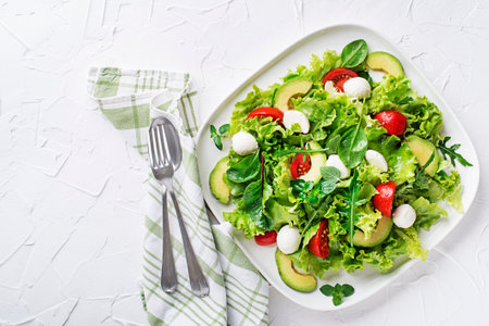 Fresh green salad with avocado, mozzarella cheese and tomato on white table backgroundの写真素材
