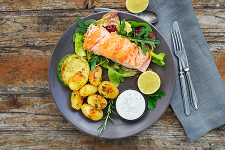 Baked salmon fillet with potatoes and vegetables on wooden table in the garden summer timeの写真素材