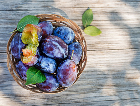 Basket of fresh ripe plums on a wooden background outdoors on sunny day.の写真素材
