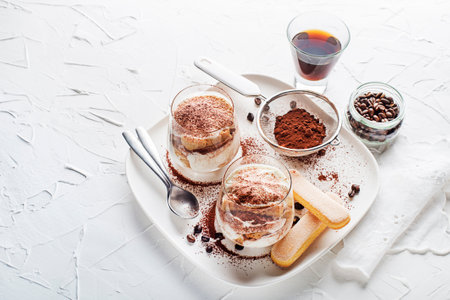 Traditional Italian dessert tiramisu in a glass cup. Homemade tiramisu in glass cup, step by step cooking process. Traditional unbaked Italian dessert on white background. Coffee and mascarpone creamの写真素材