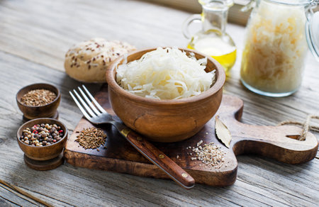 Homemade sauerkraut with black pepper and cumin seeds in wooden bowl on rustic background.