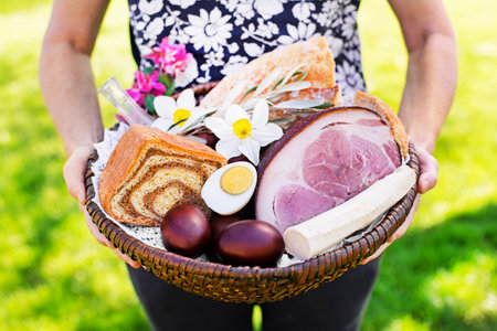 Woman holding Easter basket with traditional food. Holidays background outdoor. Easter basket filled with all sorts of delicious delicatessen ready for an Easter meal.の写真素材