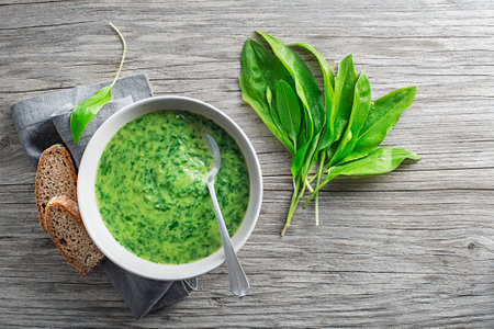 Healthy creamy soup with fresh ramson or wild garlic leaves on wooden background. Healthy spring food conceptの写真素材