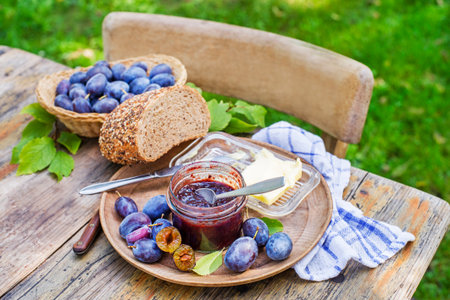 Plum jam or marmalade in a glass jar with plums fruit around outdoors on sunny dayの写真素材