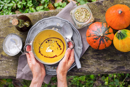 Woman served pumpkin soup with creamy silky texture. Selective focus on the pumpkin soup and hands. Outdoors in the gardenの写真素材