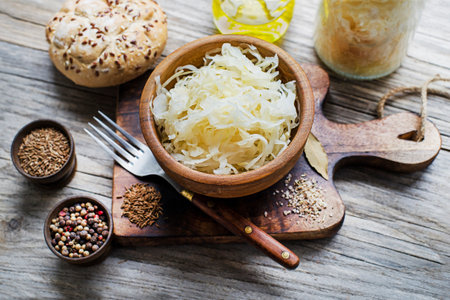 Homemade sauerkraut with black pepper and cumin seeds in wooden bowl on rustic background.の写真素材