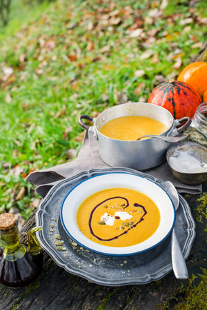 Pumpkin soup with cream and seeds in garden table surrounded by autumn leavesの写真素材