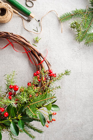 Making Christmas wreath from natural branches of spruce, juniper and holly red berries. Decorations for christmas wreath at homeの写真素材