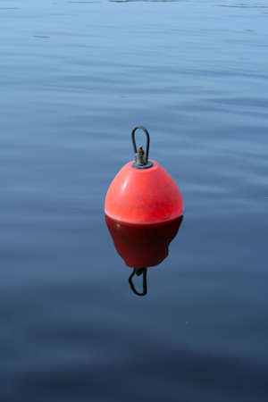 red-orange plastic buoy with iron loop on the blue waterの写真素材