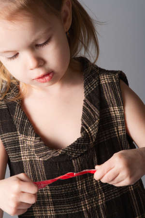 Little beauty girl look at red ribbon in her hands. She lowers her long black eyelashes.の写真素材