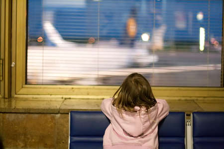 Little girl at the window in airport at night. Airplanes not in focus.
