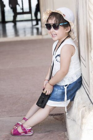 Portrait of a happy little girl laughing and leaning on the wall outdoors.の写真素材