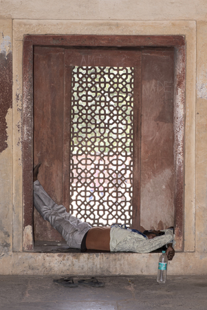 Fatehpur Sikri, India - October 12, 2016: Tired man sleeps on a lattice window during daytime at Jodha Bais Palace in Fatehpur Sikri, Agra, India.のeditorial素材