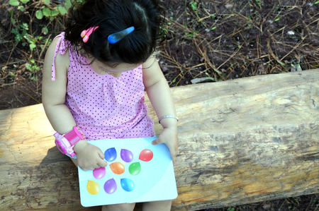 Toddler reading a book outdoors. Sitting on a log head down.の写真素材