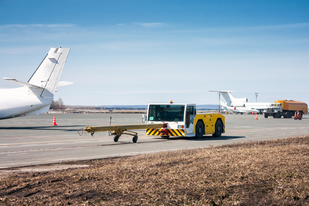 Tow tractor with towbar and tank truck aircraft refuelers moves at the airport apronの写真素材