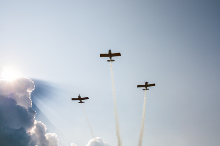 Three sports airplanes in flight releasing smoke against the background of a cumulus cloud because of which the sun shinesのeditorial素材