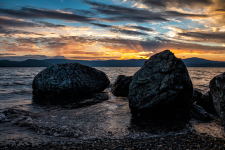 Large blocks of stones on the shore of the lake against the backdrop of a beautiful sunsetの写真素材