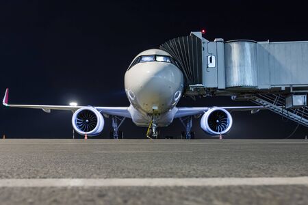 Front view of a white passenger aircraft connected to an external power supply on an airport night...