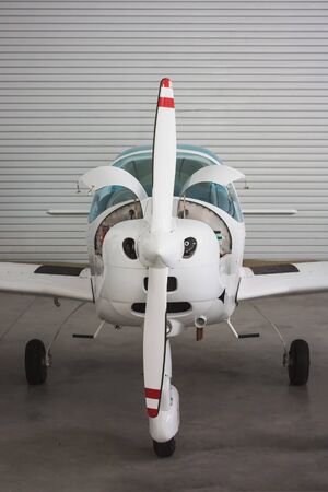 Close front view of a small white sports plane in a hangar. The aircraft has an open engine