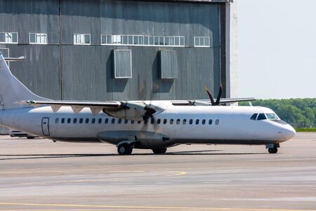 Taxiing white passenger turboprop airplane at the airport apron near hangar