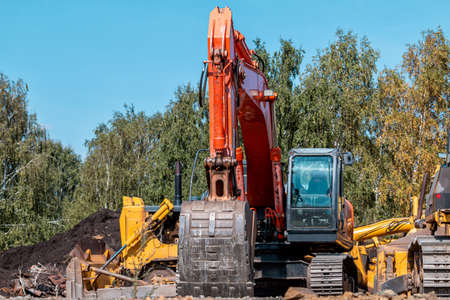 Close-up orange crawler excavator and two yellow bulldozers during repair work near the forest