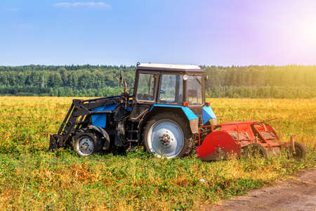 Modern wheeled agricultural tractor with harvesting equipment on an field