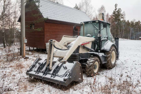 White wheeled tractor excavator on the snow near the forest in winter