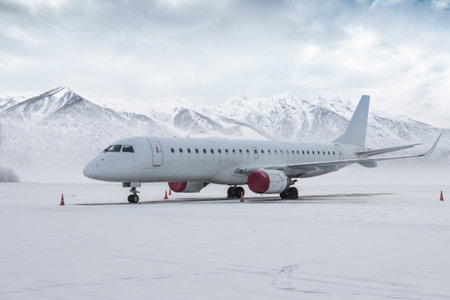 White passenger aircraft on the airport apron in a snowstorm on the background of high scenic...