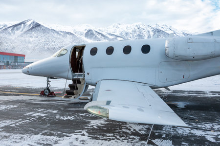 Close-up of the modern white business jet with an opened gangway door at the winter airport apron on the background of high scenic snow capped mountainsの写真素材