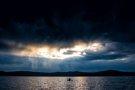 Storm clouds over the lake. Silhouette of a SUP boarder on the water