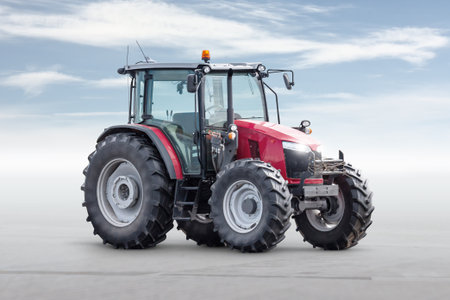 Red modern wheeled tractor isolated on bright background with sky