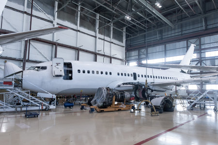 White passenger airplane under maintenance has opened weather radar and engine removed located nearby in the aircraft hangarの写真素材